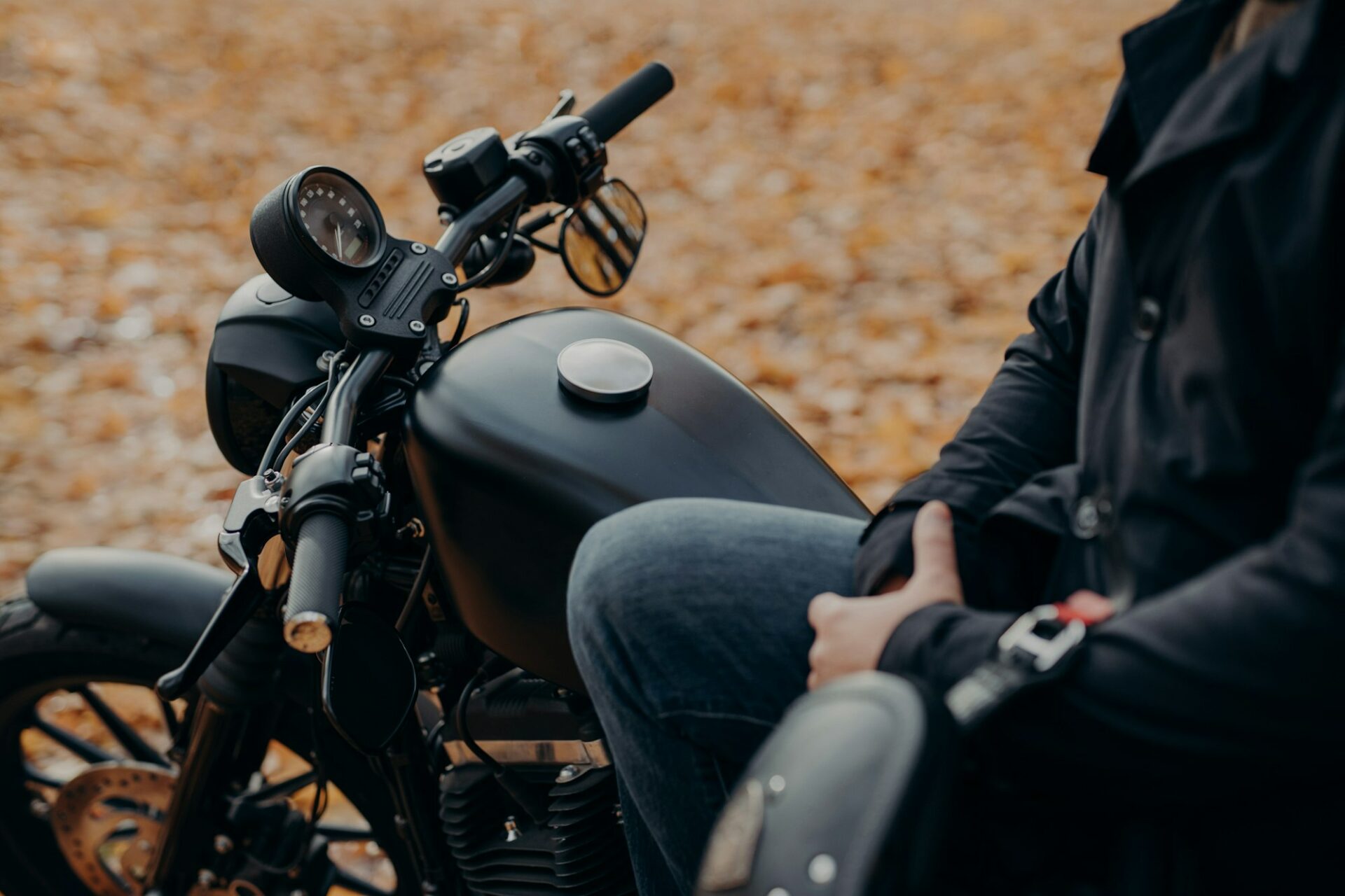 Faceless biker poses on fast motorbike, stops in park, ground covered with fallen leaves